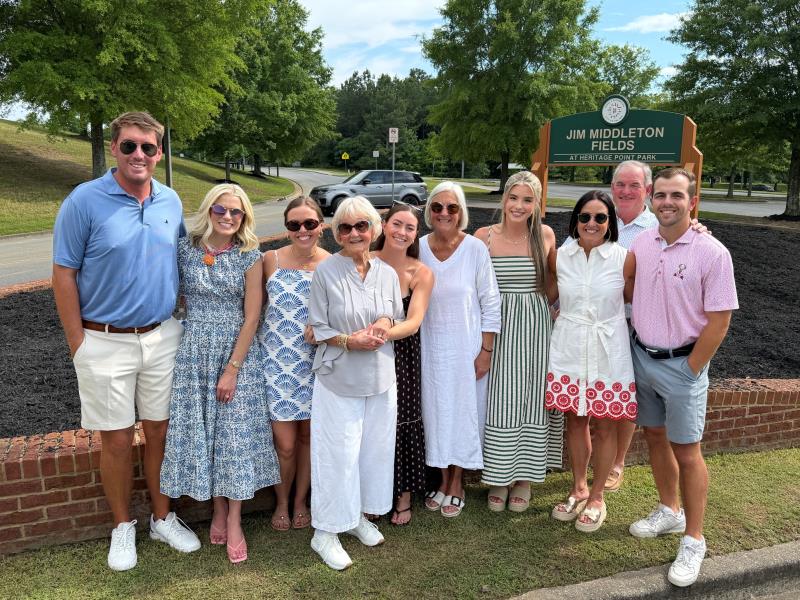 Members of the Middleton family posed together for a picture in front of the newly unveiled sign for the Jim Middleton Fields at Heritage Point Park on Friday